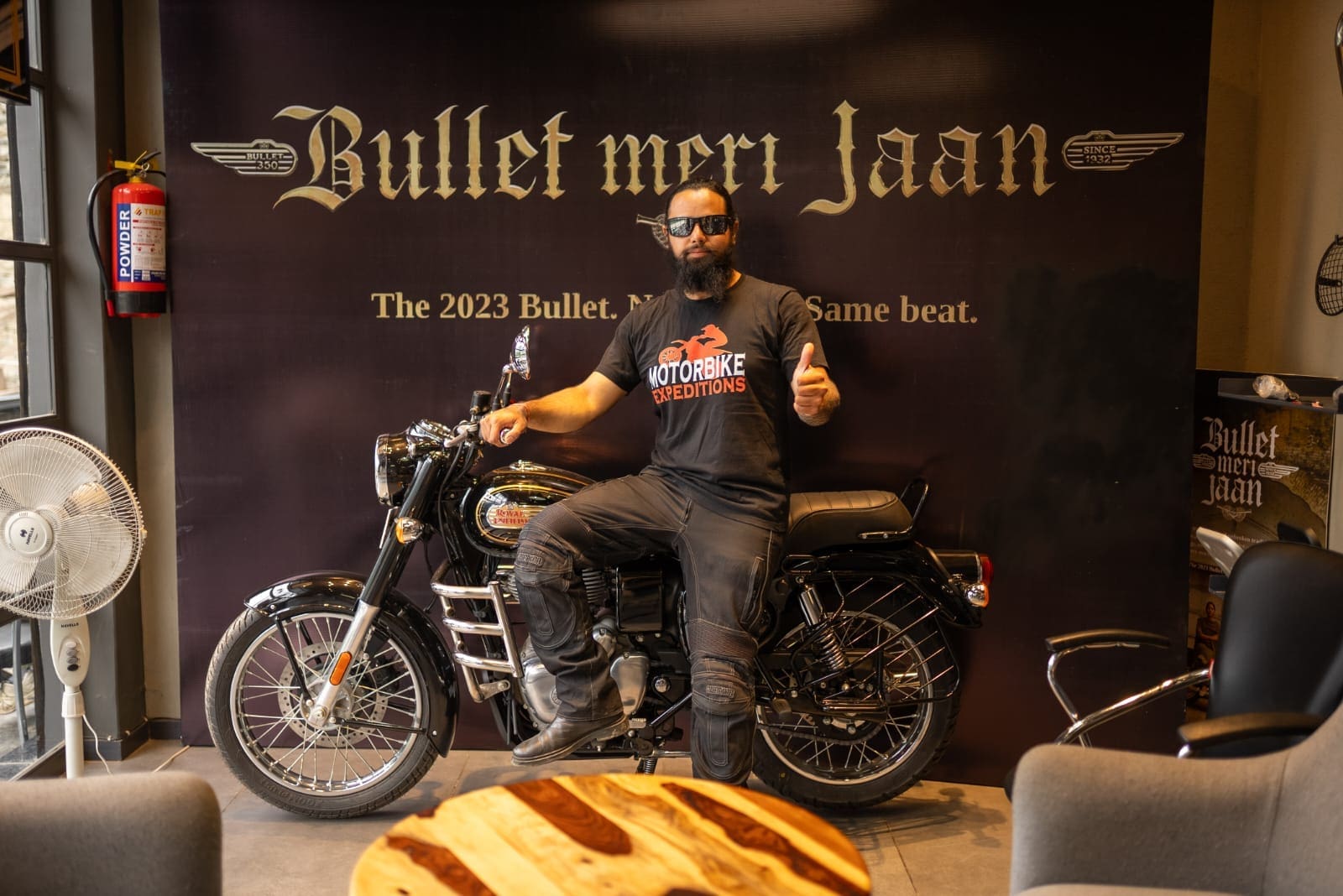 akshay is at RE shop and sit on the bike with backround "bullet meri jaan"