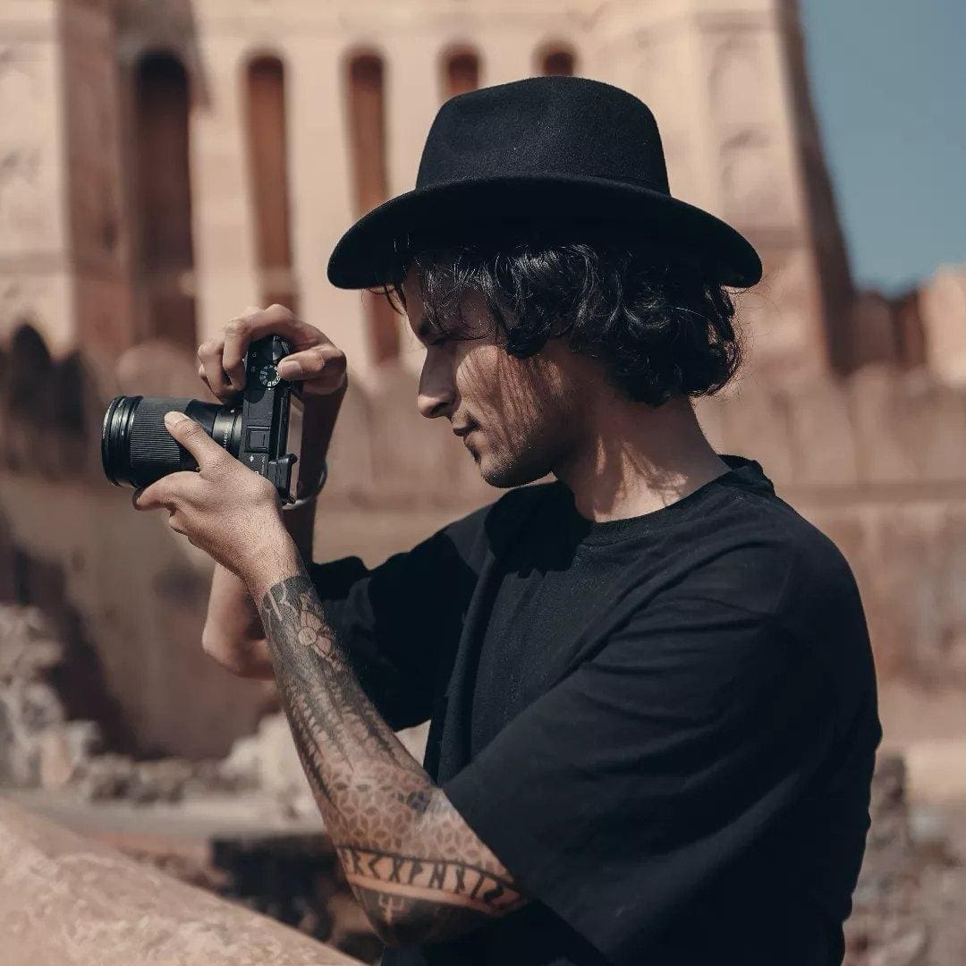 Videographer in black attire and hat using a professional camera outdoors.