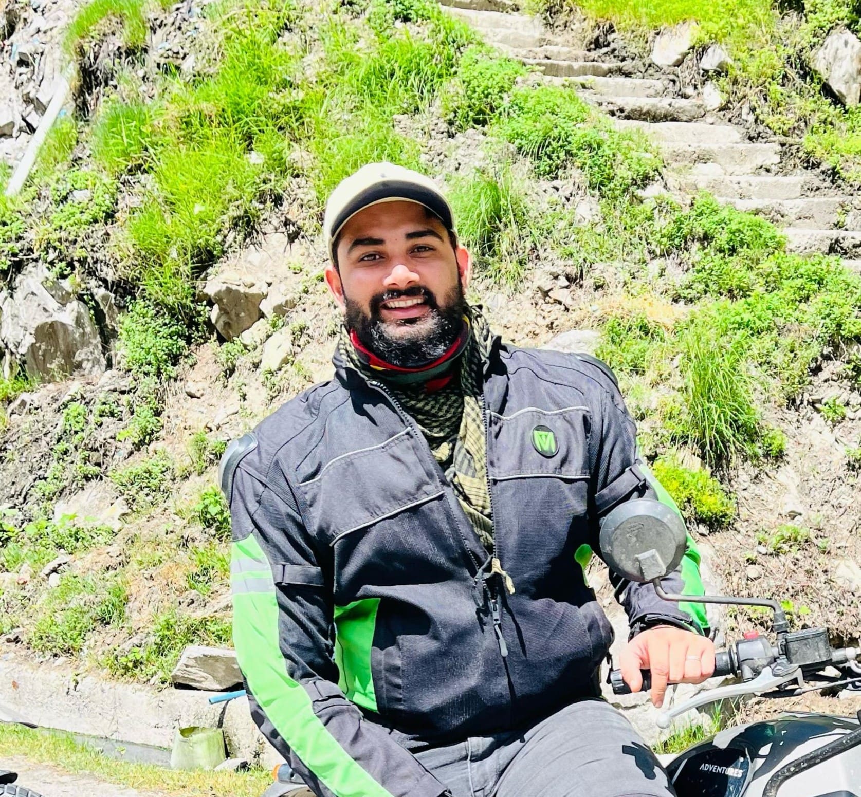 Motorbike tour guide smiling on a mountain trail with lush greenery in the background, illustrating a sense of adventure and expertise in outdoor excursions.