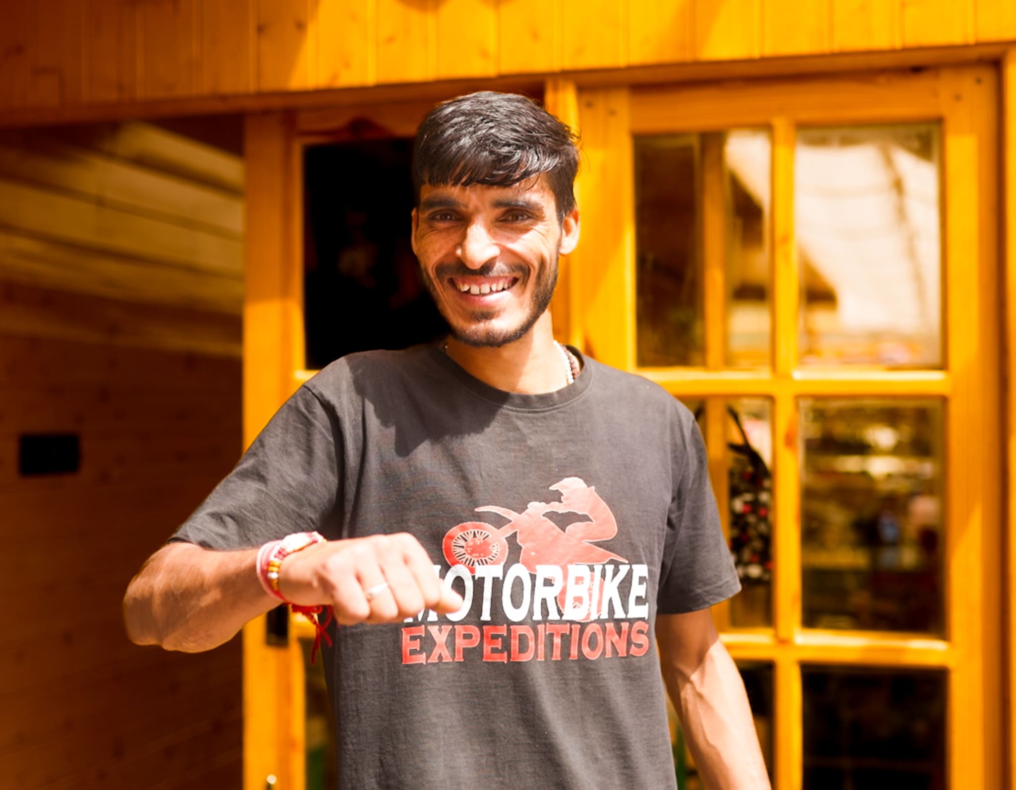 Khushwant, a mechanic at Motorbike Expeditions, smiling in front of a wooden lodge, representing the company's commitment to excellent customer service and expertise in motorbike maintenance.
